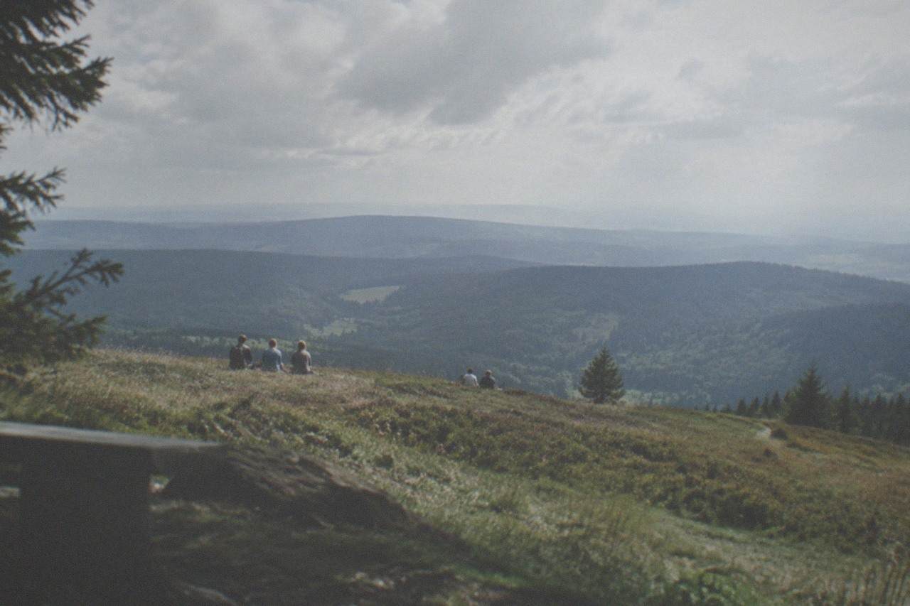 Open grassy summit ridge with distant forested hills under a partly cloudy sky