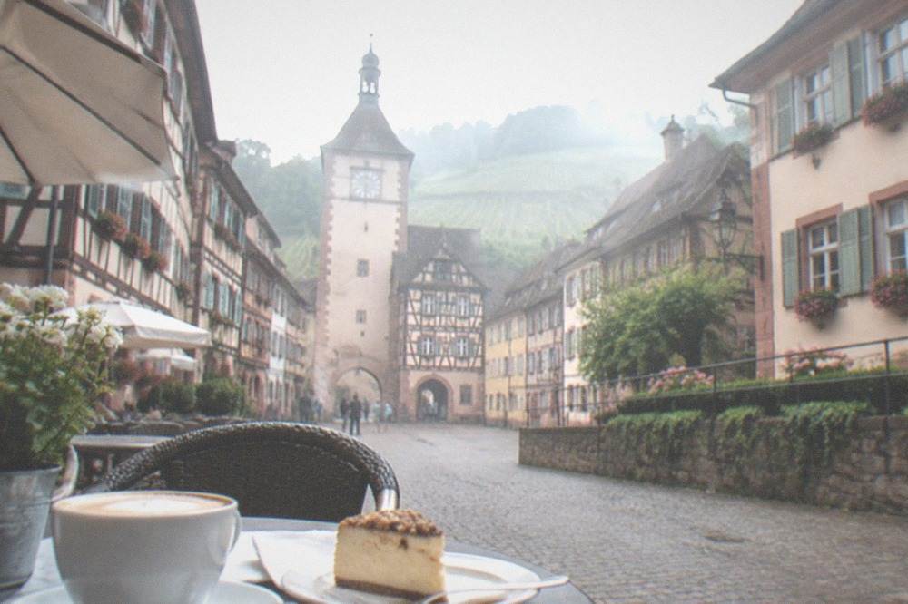 A café table with coffee and cake beside an old town lane