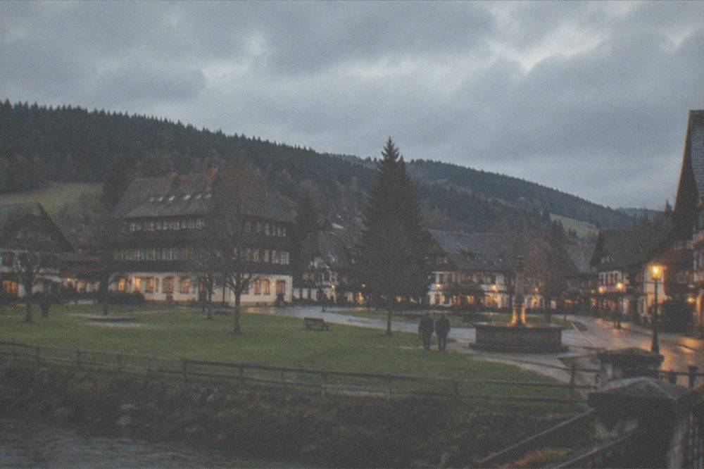 A lantern-lit old town street with timbered facades and a lit fountain at dusk