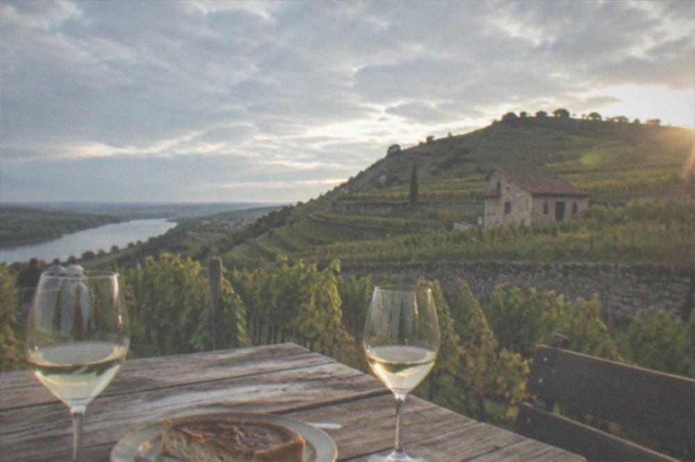A rustic tavern table with a slice of onion tart and two glasses of pale wine