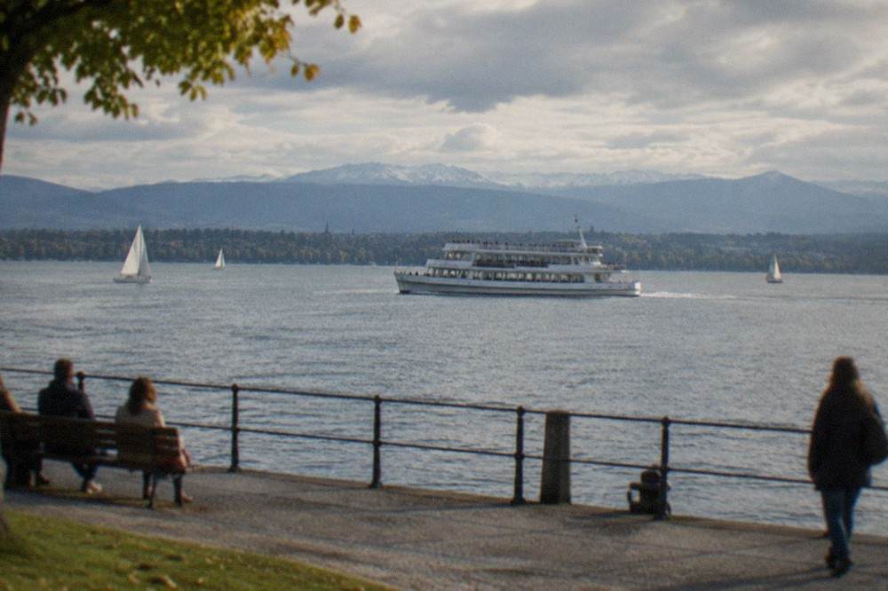 White passenger ferry crossing blue lake water with hills in the background