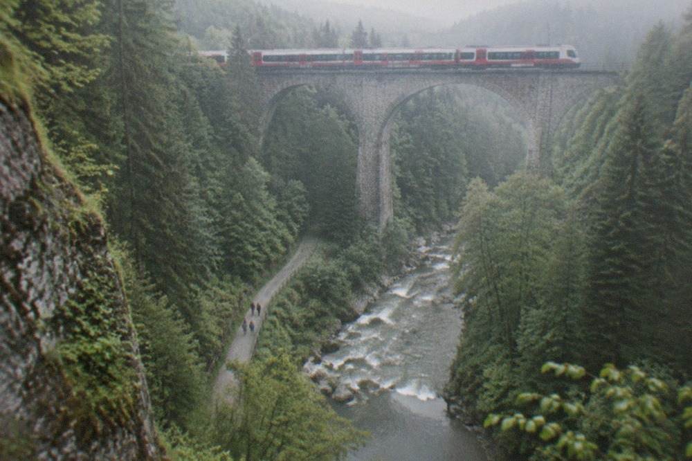 Regional train crossing a stone viaduct above a forested gorge