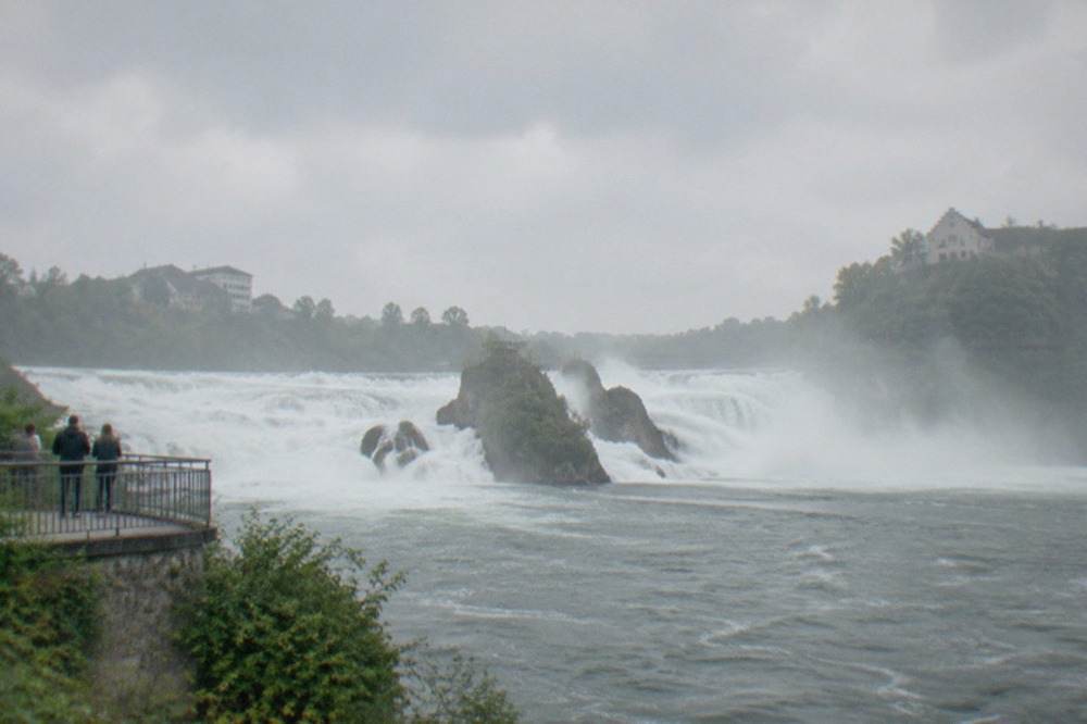 Fast grey river water surging over a wide rock ledge and dropping into a churn below