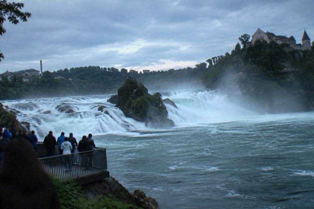 Viewing platform crowded railings above a broad waterfall with mist rising from the plunge pool