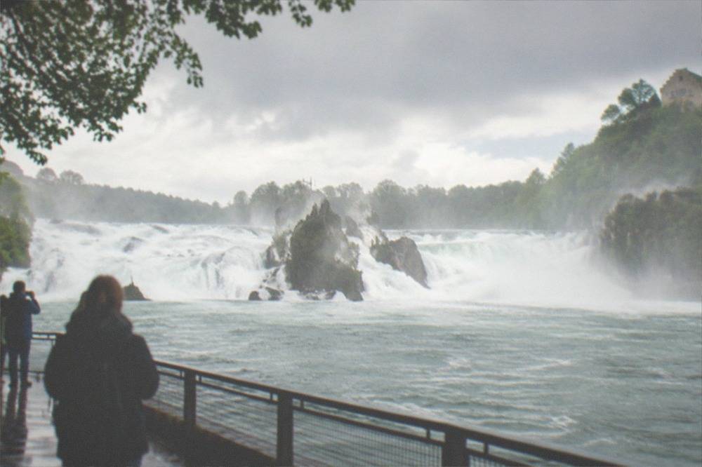 Waterfall in full spring flood with dense white water and mist drifting over green banks