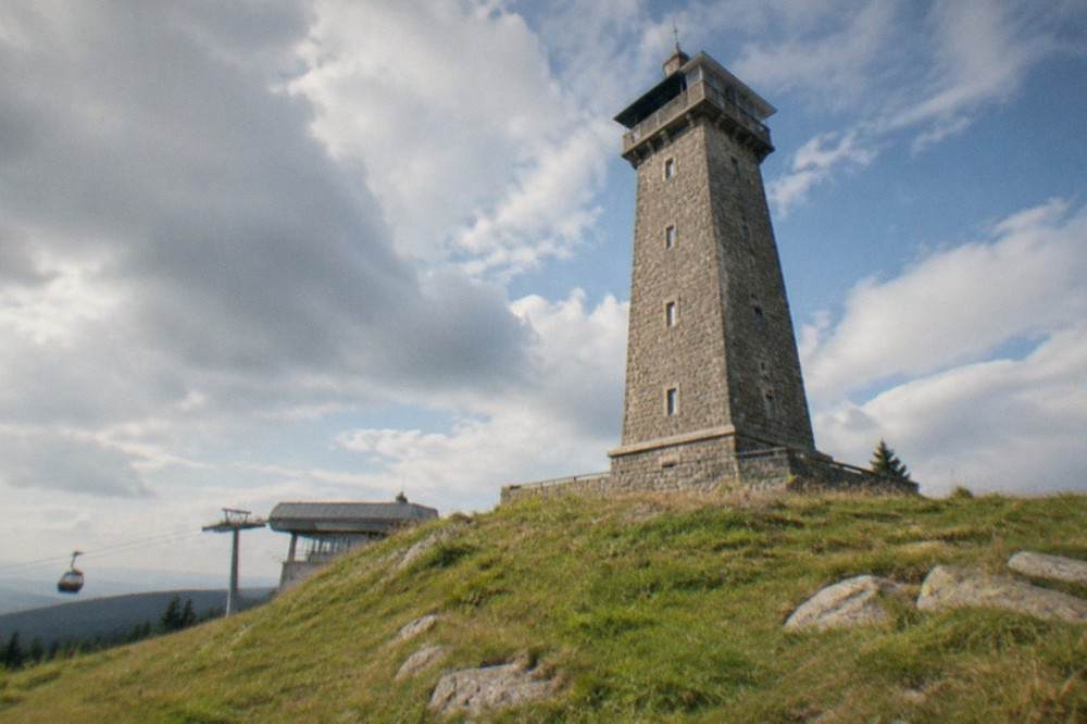 Stone observation tower on an open mountain meadow above forest