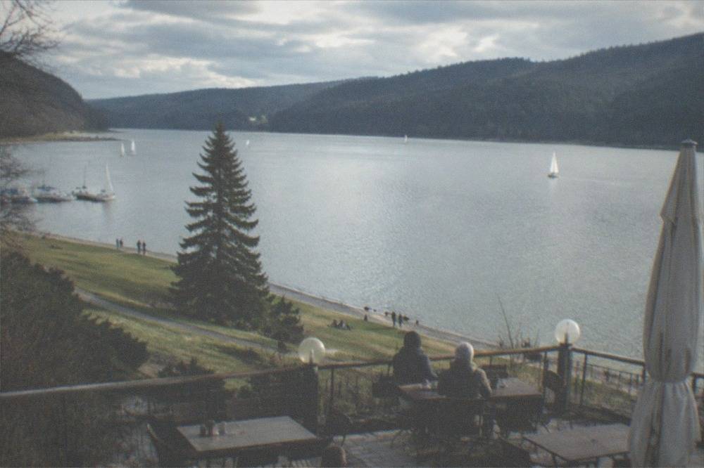 A lakeside terrace with tables and chairs looking out over quiet water in late afternoon light