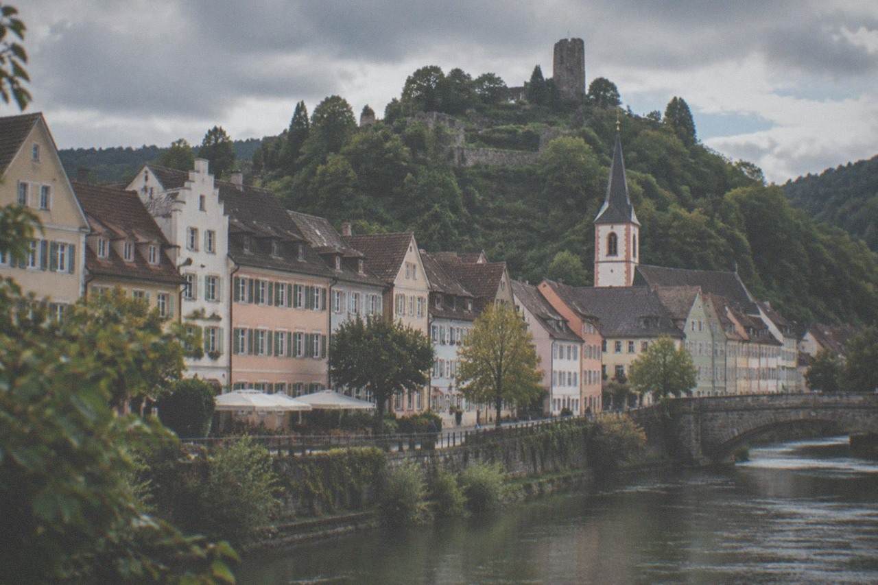 Pastel facades of old town houses rising toward a green hilltop with castle ruins above a small German wine town
