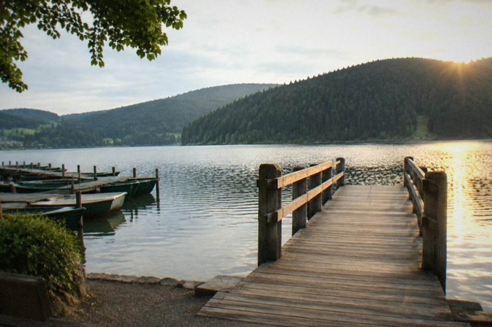 A wooden pier extending over calm lake water toward forested slopes