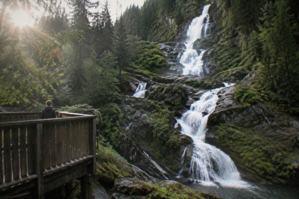 A wooden viewing platform beside a narrow cascade in a green gorge