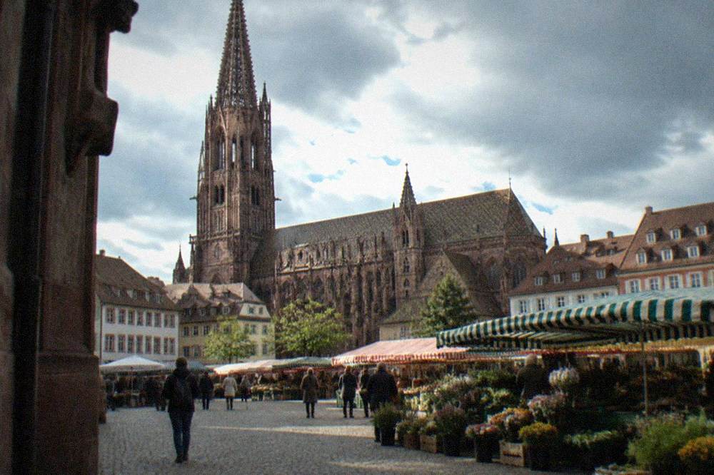 A market square with striped stall awnings and a gothic cathedral tower above the roofs