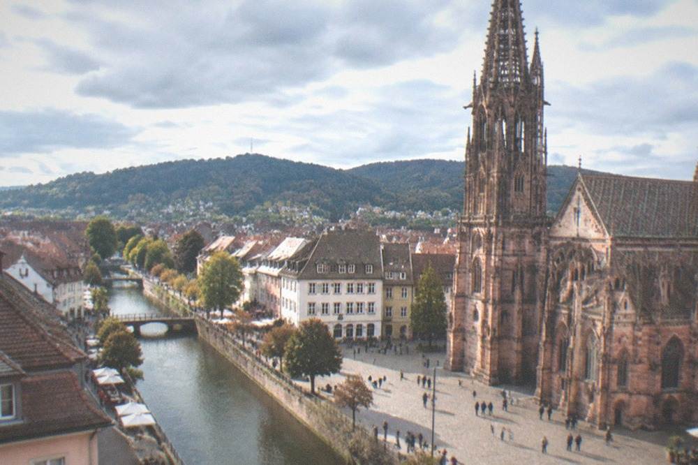 Visitors strolling along a sunlit Freiburg canal street lined with cafes