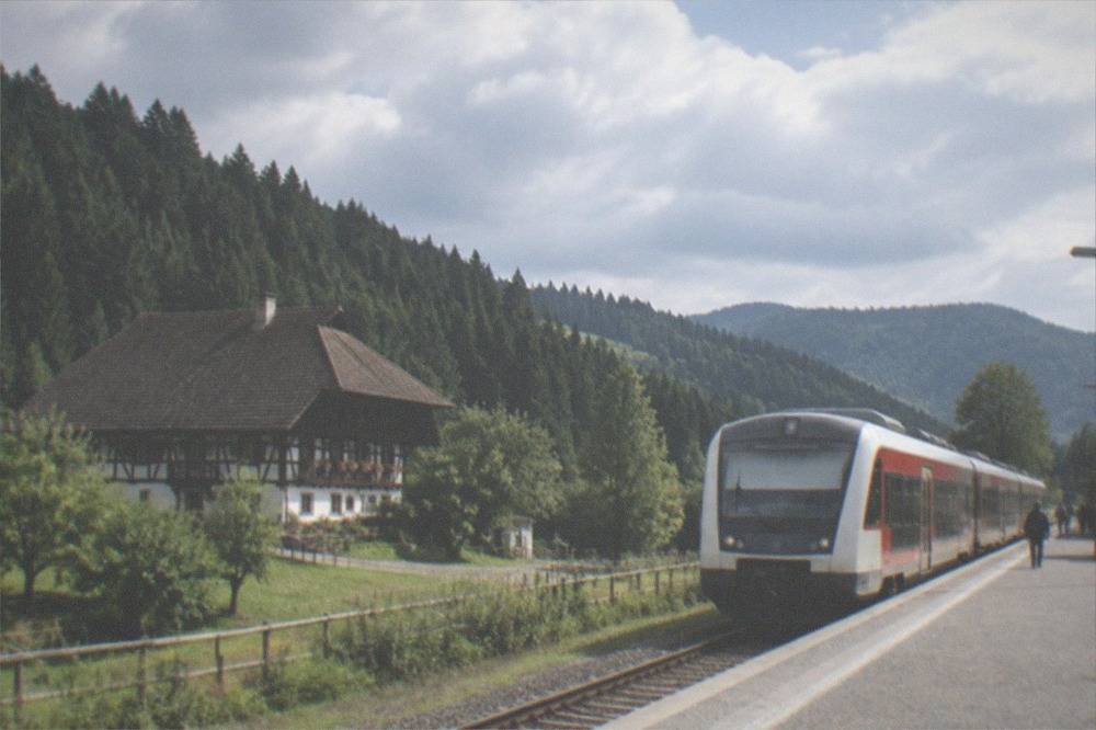 Regional train waiting at a small Black Forest station with forested hills behind the platform.