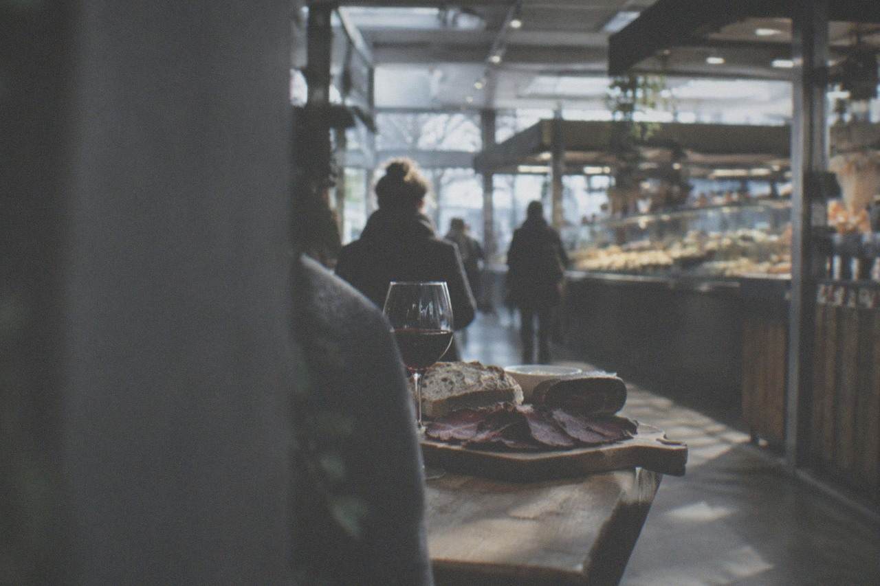 Slices of dark smoked ham arranged on a wooden board beside bread and a glass of red wine