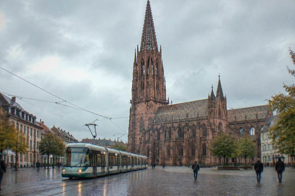 Freiburg tram moving through a city street with the cathedral tower behind