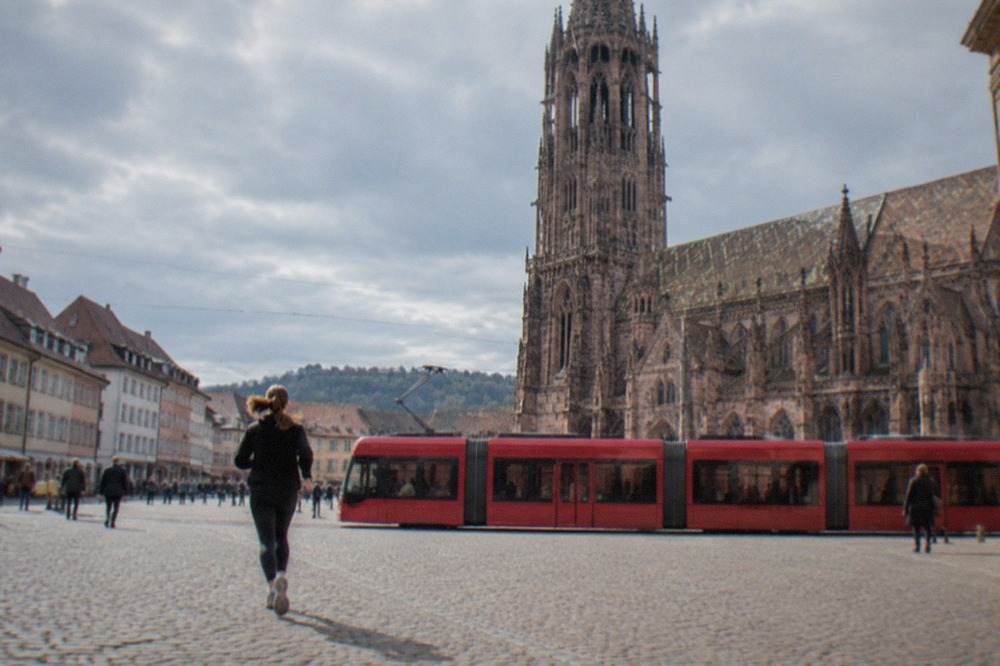 A red tram crossing a cobblestone square in front of a Gothic cathedral tower in Freiburg