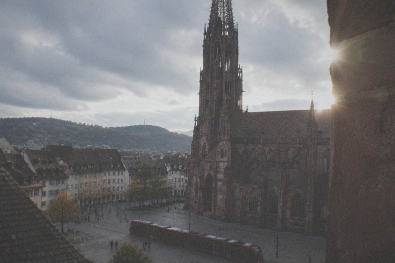 A red tram crossing a cobblestone square in front of a Gothic cathedral tower in Freiburg