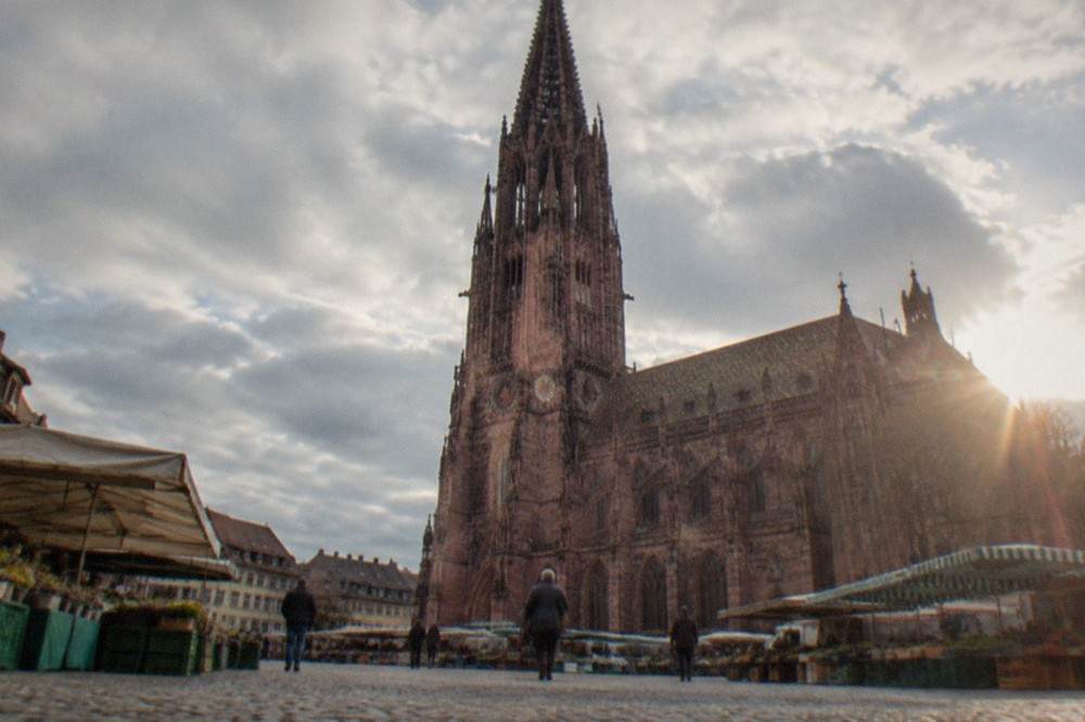 Market stalls spaced along the flat paved square beside Freiburg minster in morning light