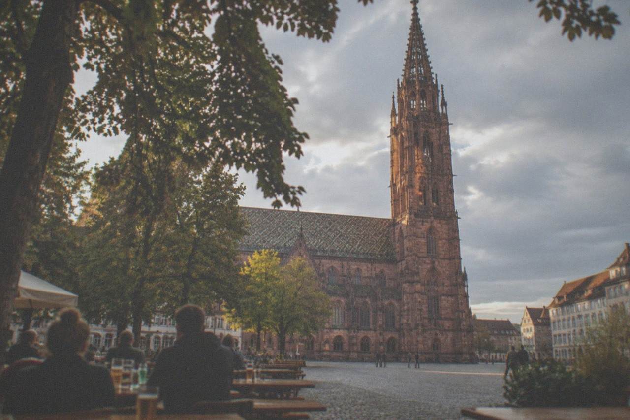 Wooden beer garden tables with drinks under chestnut trees beside a historic Freiburg square