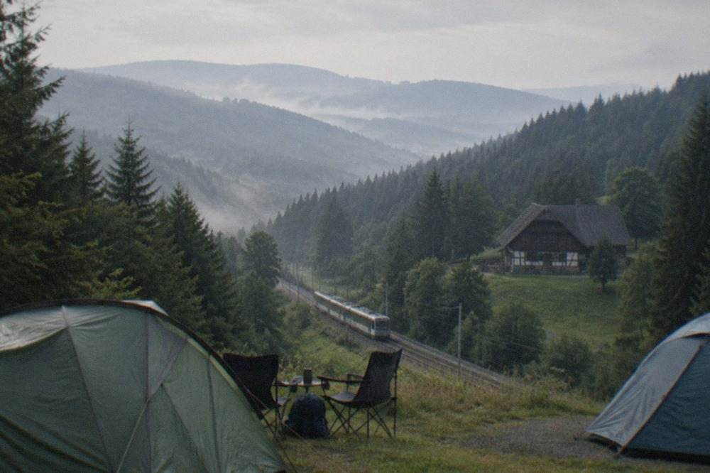 Campsite pitch at dawn with a tram line and Black Forest hills visible beyond the tents