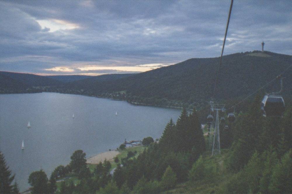 Cable car cabins rising over green forest slopes toward a mountain summit with an observation tower