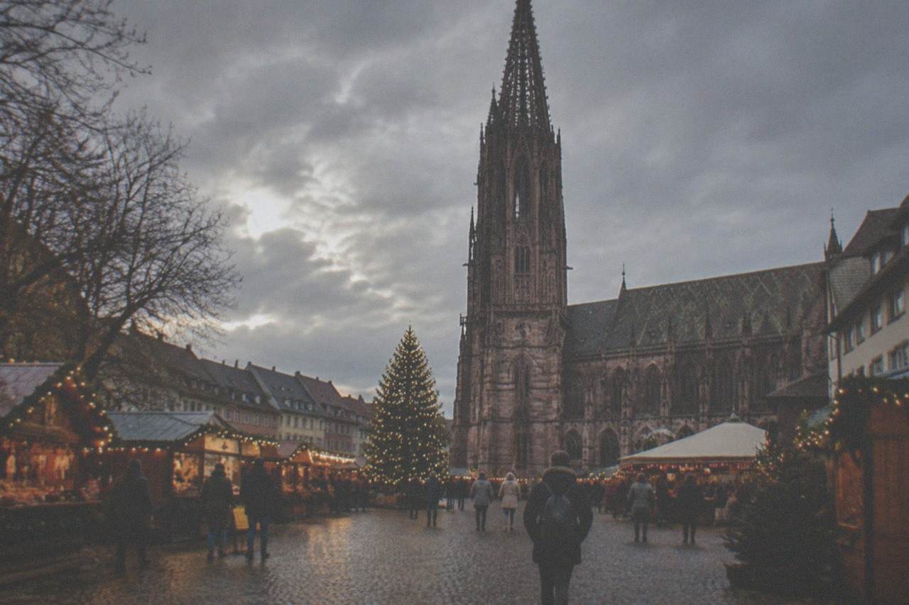 A Christmas market square in Freiburg at dusk with wooden stalls and a lit tree