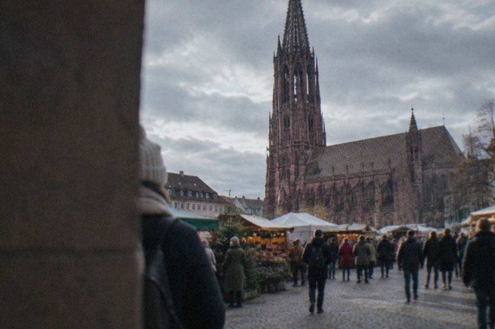 Crowded market square in Freiburg with festival stalls and the gothic minster tower behind