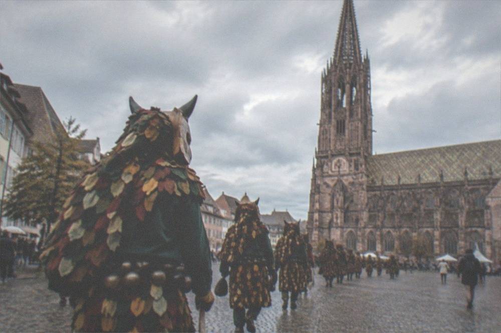 Costumed carnival figures with carved wooden masks parading through a Freiburg street