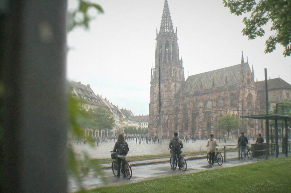Commuters with bicycles waiting at a grass-lined Freiburg tram stop