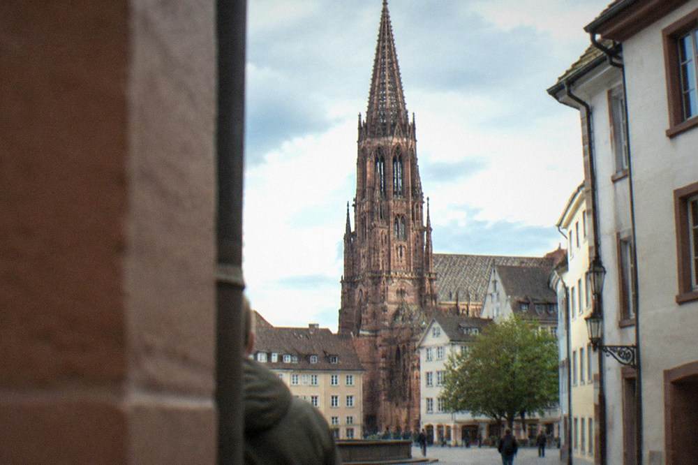 Red sandstone minster tower and spire above rooftops seen from a nearby street