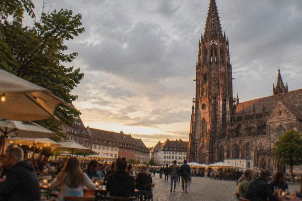 Lit pub gardens and crowded tables on a Freiburg square at dusk
