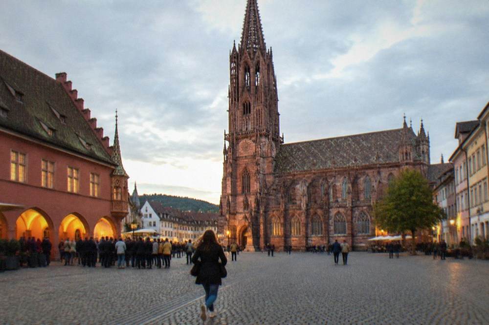 A small crowd gathered at dusk outside a lit Freiburg old town building