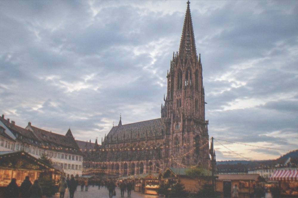 A Freiburg square at dusk with market lighting strung between timber stalls