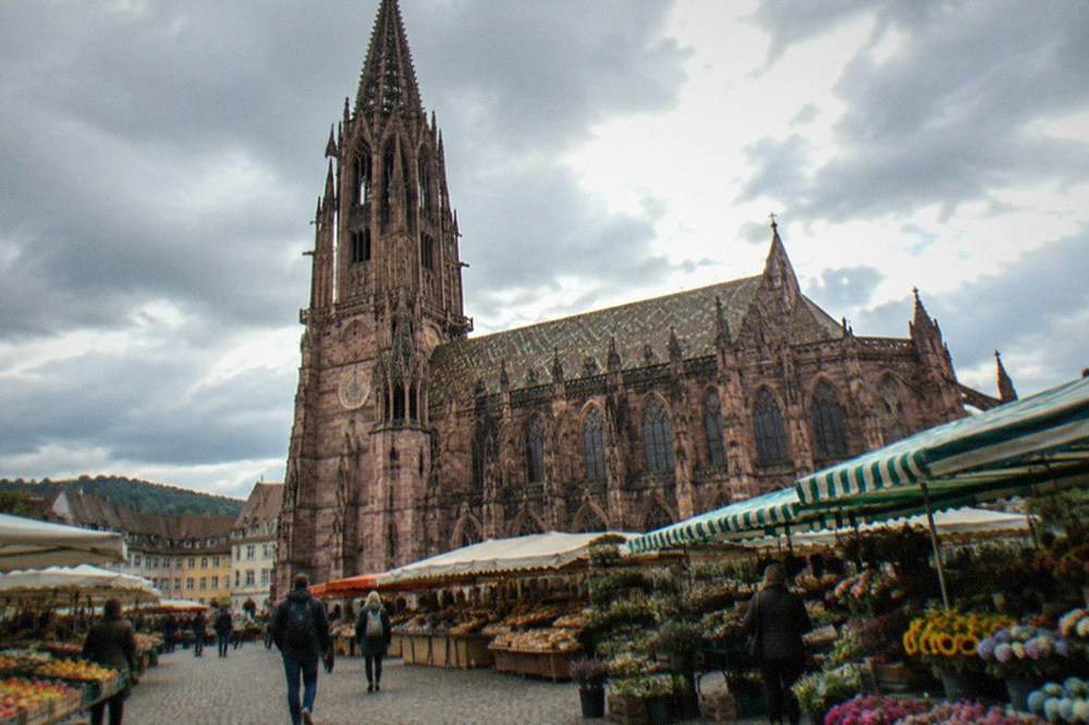 Market stalls with fruit, flowers and bread beside a Gothic stone cathedral in Freiburg