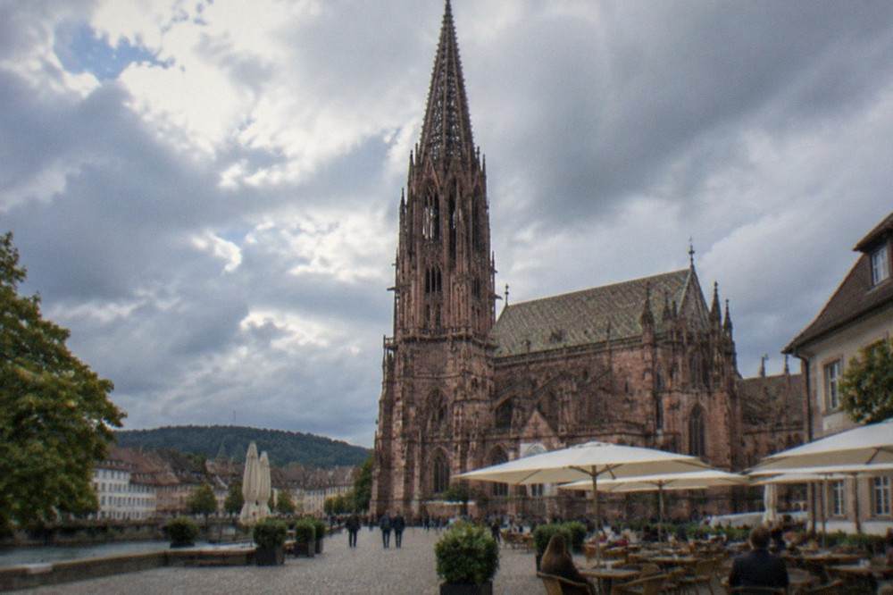 Outdoor café tables on a cobbled square beside the Freiburg Münster