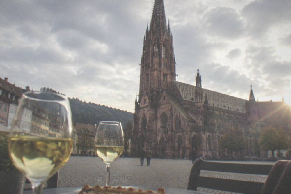 Outdoor table with glasses of white wine and a slice of onion tart