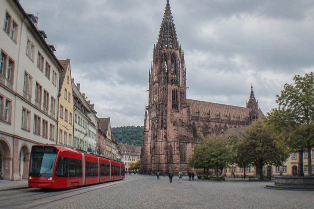 A red tram traveling along a track beside historic buildings in central Freiburg
