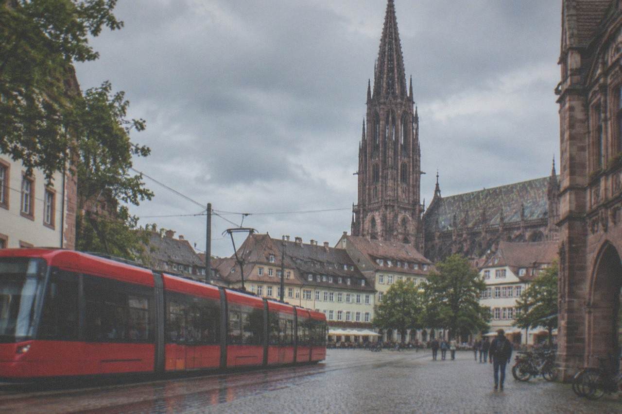A red Freiburg tram passing through the old town with the Minster spire behind the rooftops