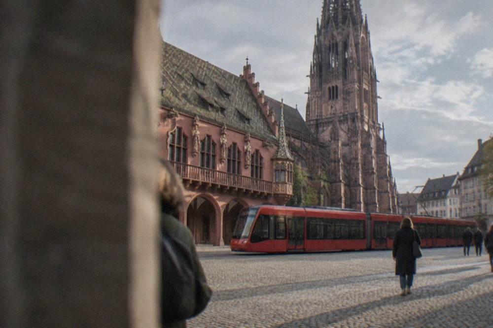 A red Freiburg tram passing the historic Kaufhaus facade on a sunny street
