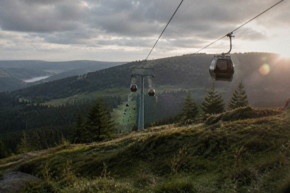 Cable car cabins traveling up a green mountain slope toward a forested summit