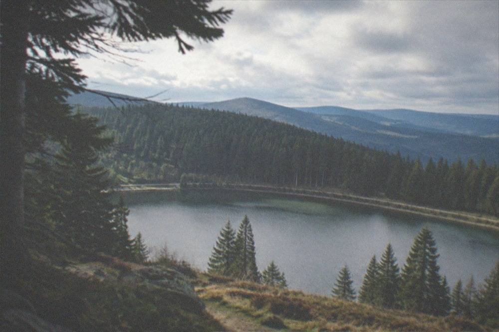 Small mountain lake surrounded by dark fir forest with a promenade along the shore