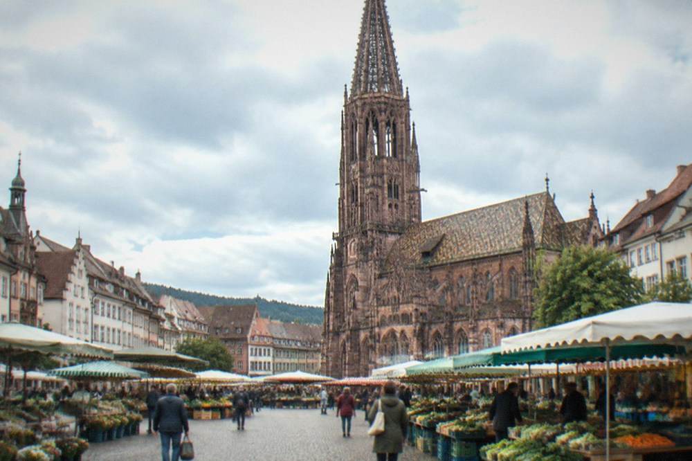 Market square in a Freiburg district with fresh produce stalls and shoppers under morning clouds