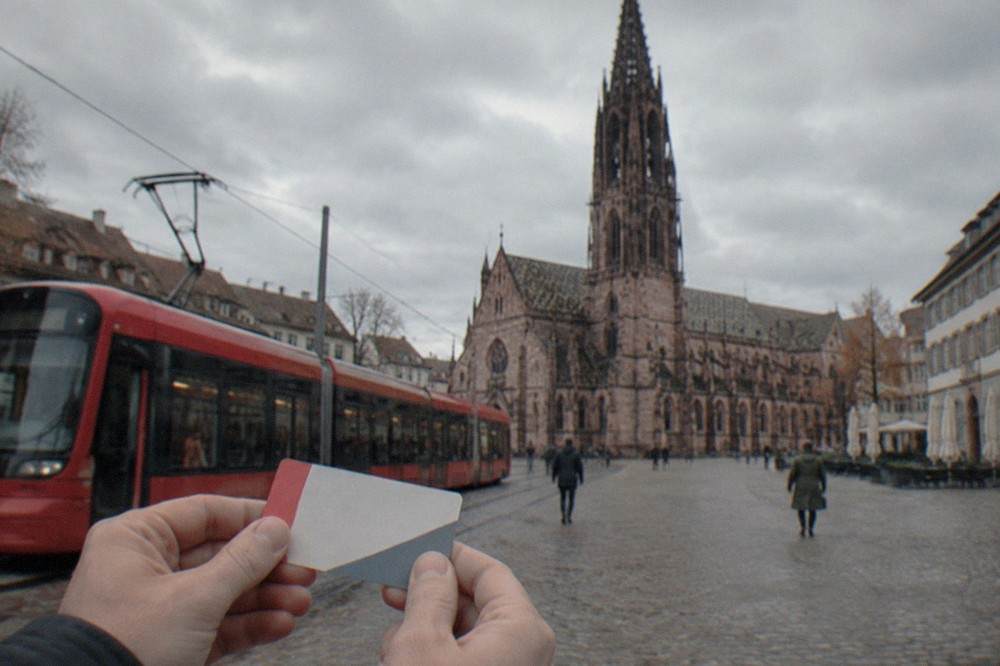 Hands holding a paper transport card in front of a red Freiburg tram at a stop in the old town