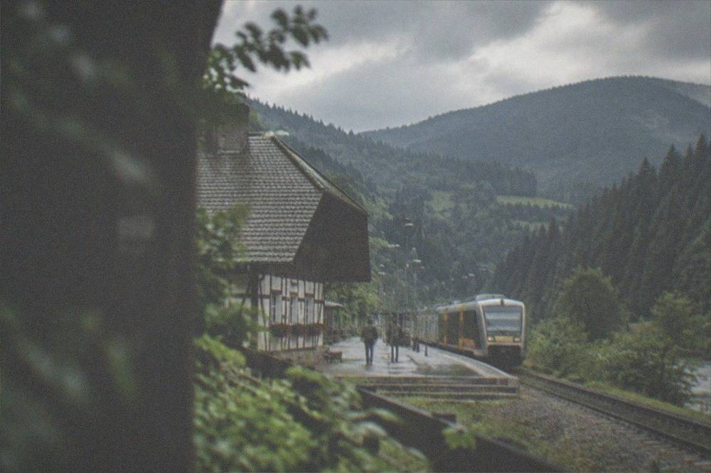 Regional train at a small Black Forest valley station with forested hills behind the platform
