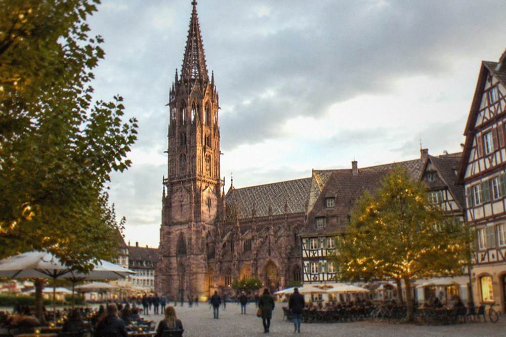 An evening square with lit trees, outdoor tables and half-timbered facades
