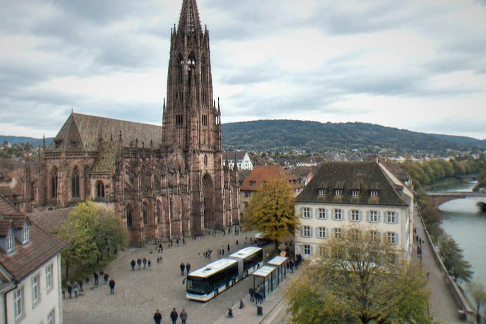 Modern electric city bus at a stop beside a Freiburg plaza with pedestrians