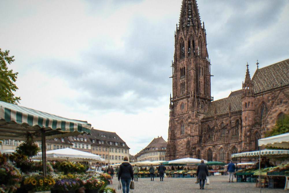 Market stalls on a historic square beside a gothic cathedral tower in Freiburg