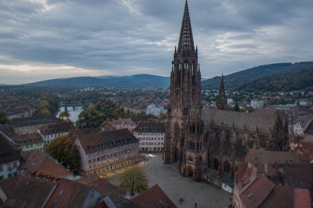 Freiburg Minster tower seen across red rooftops toward the Black Forest hills