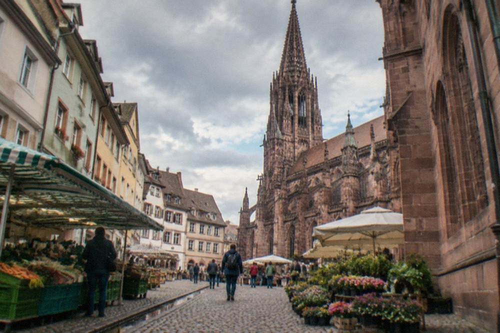 Market stalls and traders in front of a red sandstone gothic cathedral on a bright morning