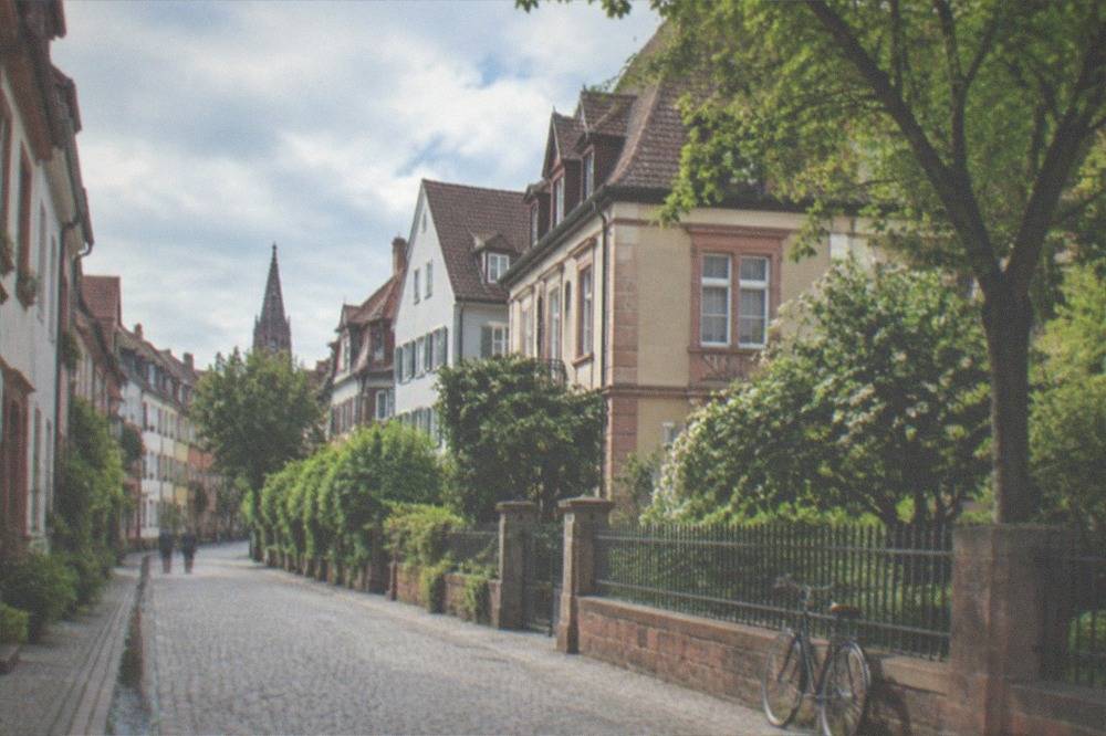 Leafy residential street with old villas and a bicycle leaning against a fence in the morning light